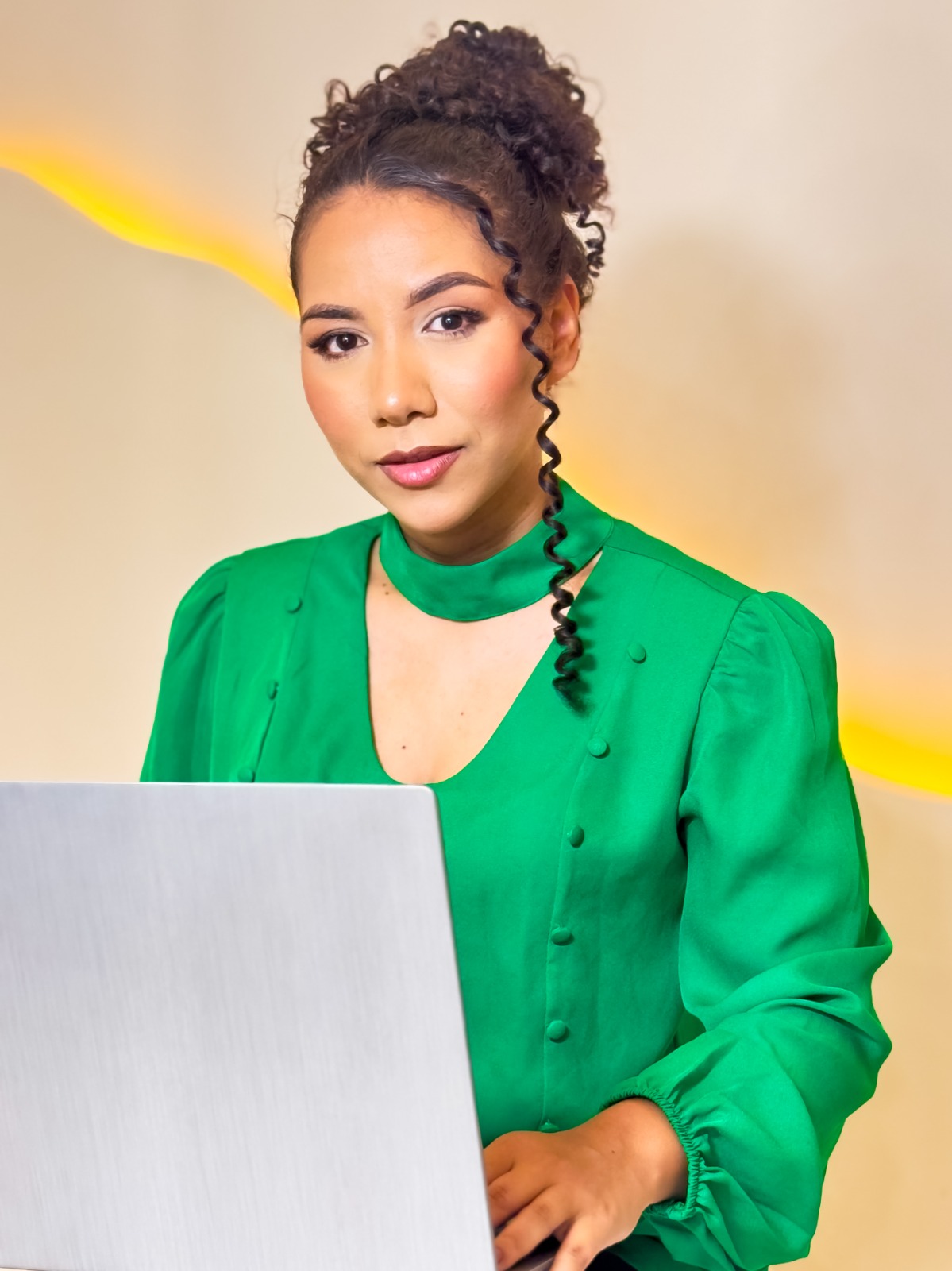 Kesia Cristina com blusa verde, sentada diante de um notebook.